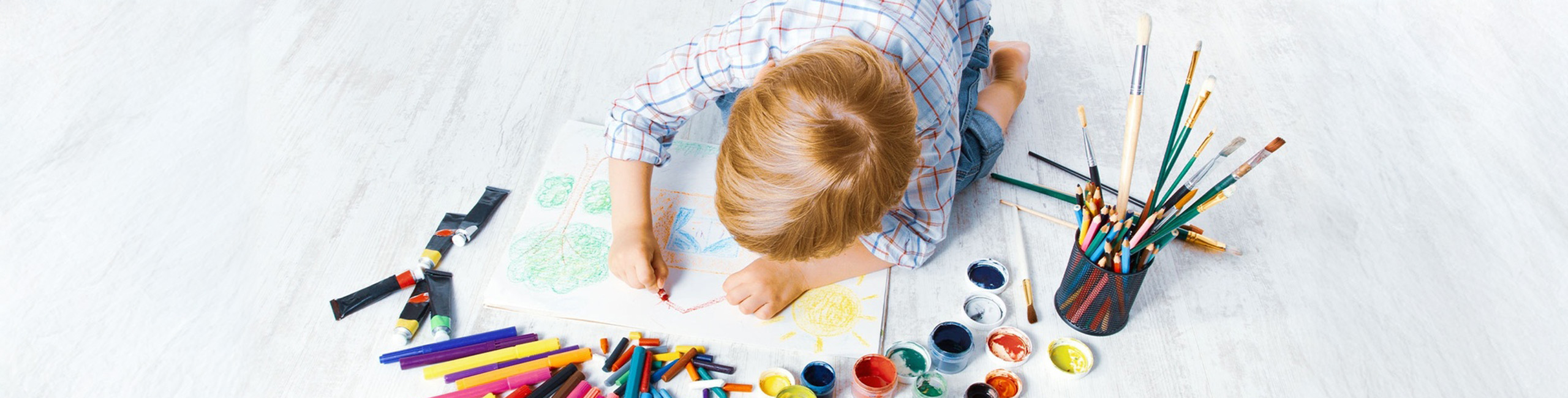 Otroc se igra z barvicami na tleh.