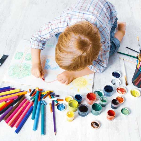 Otroc se igra z barvicami na tleh.