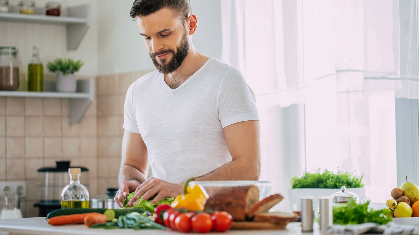 Moški športnik v kuhinji pripravlja zdrav obrok.