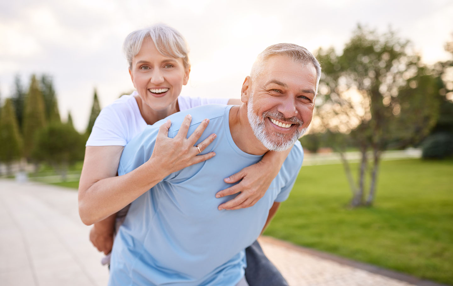 Portrait of lovely happy elderly couple on morning run outside in city park, retirees wife and husband rejoice in active lifestyle, smiling woman tenderly embracing her spouse after routine jogging